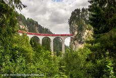 Rhätische Bahn in het Albula / Bernina landschap - Rhätische Bahn in het Albula / Bernina landschap: Een rode trein op het Landwasserviaduct bij Filisur. Het lijkt of de trein...